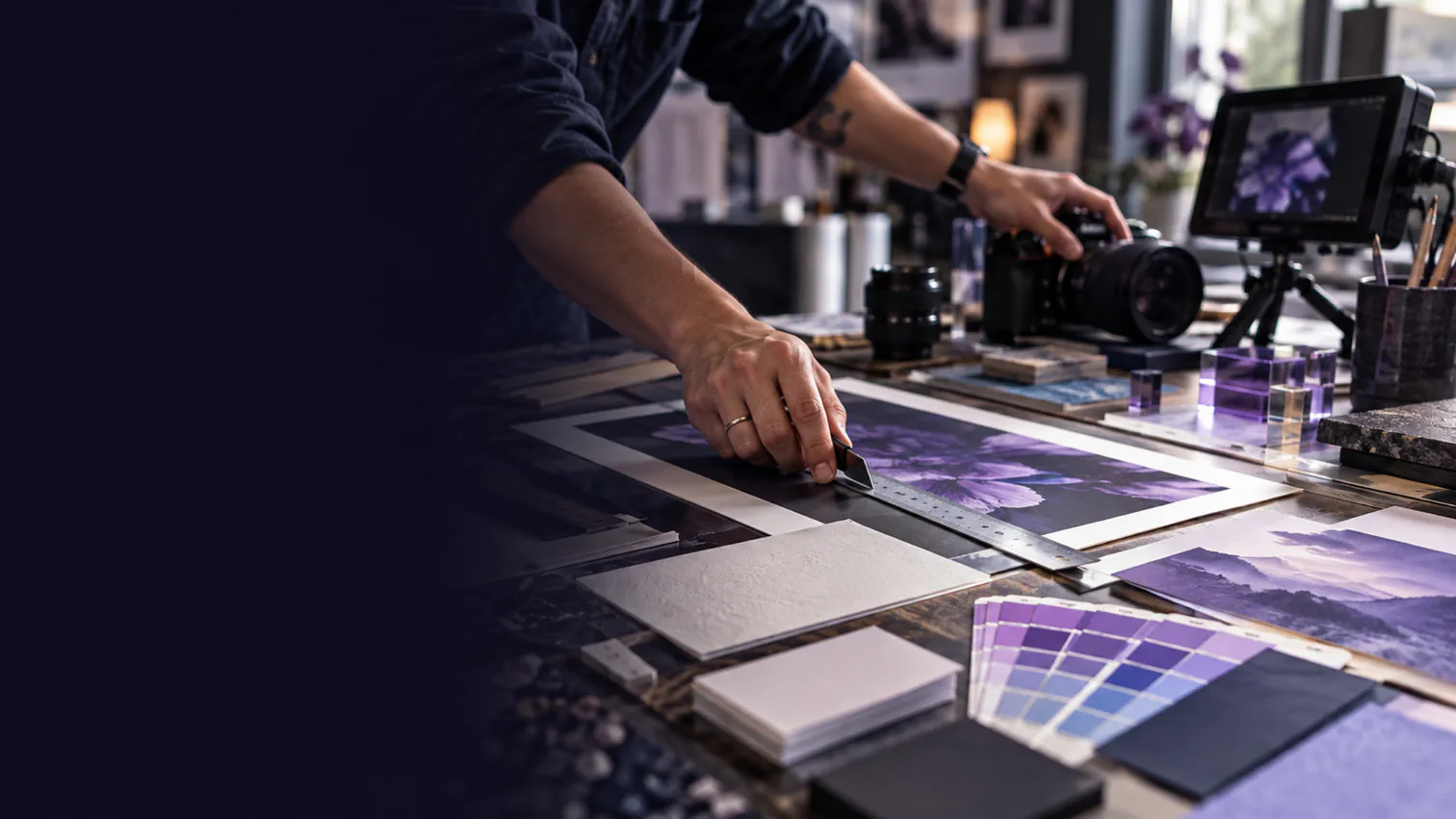 A designer trims a print proof beside professional photography and video equipment.