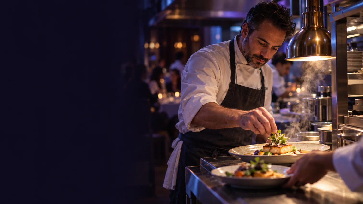 A restaurant owner-chef finishes a dish at the pass during evening service.